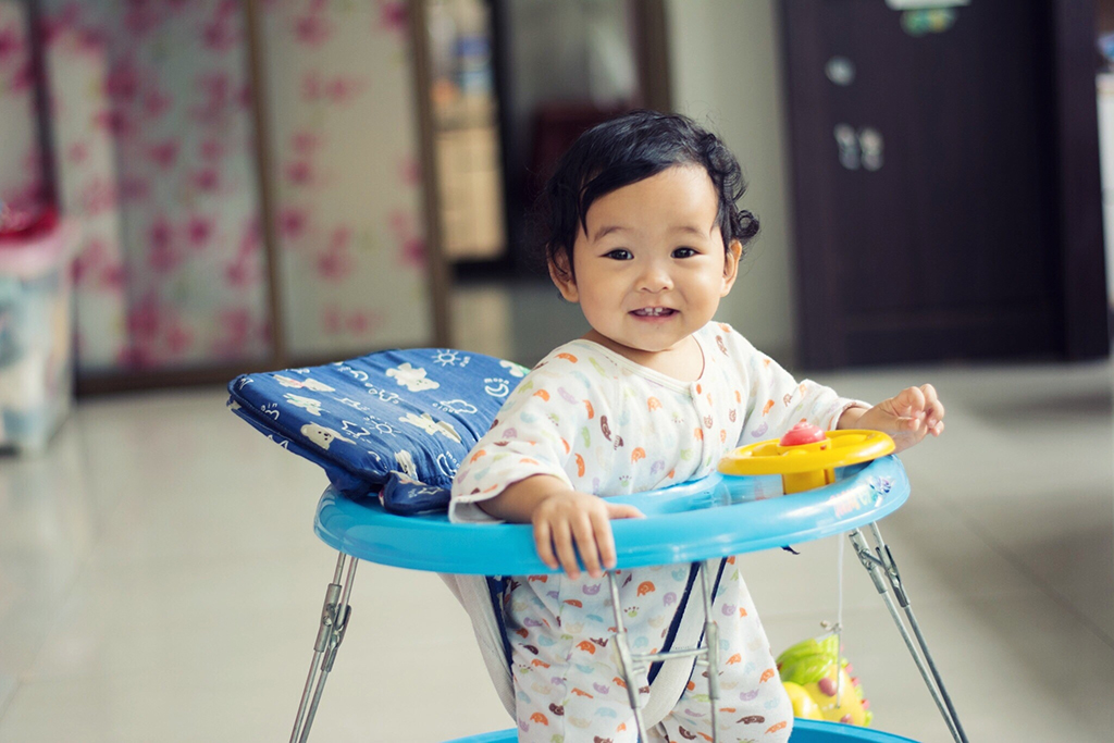 A light-skinned toddler dressed in a onesie stands in a walker