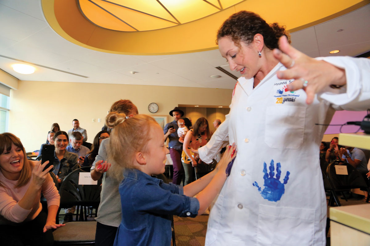 CHLA patient Ruby Chan places her handprint on Dr. Berry’s white coat during Hyundai Hope on Wheels’ signature Handprint Ceremony. The colorful markings represent patients’ journeys, hopes and dreams.