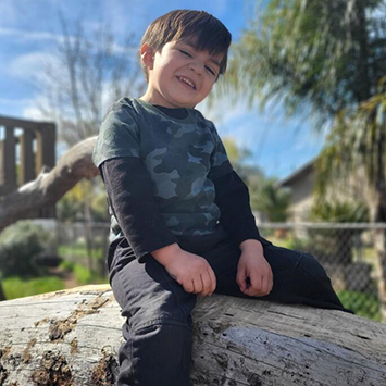 CHLA-Martin-sitting-355x355.jpg Little boy Martin smiles as he sits atop a tree branch in front of a tree house