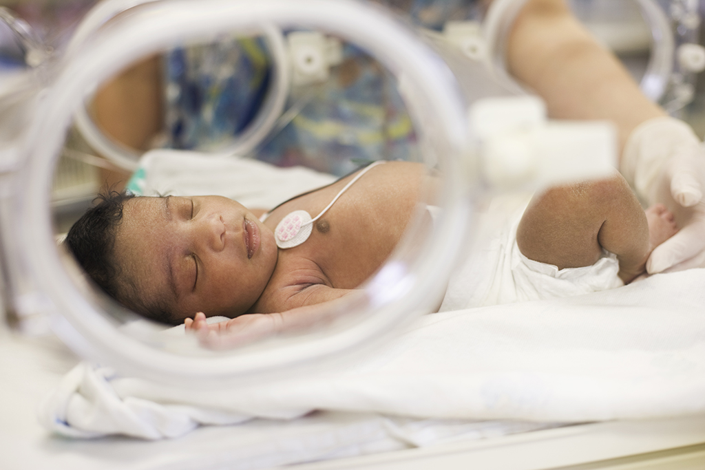 Newborn infant rests in hospital incubator