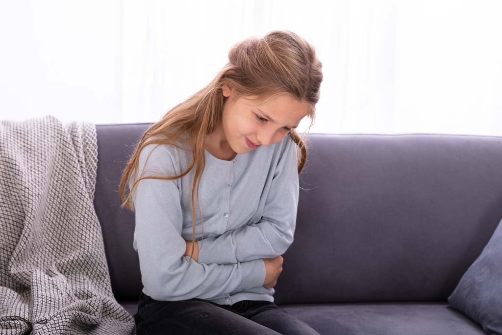 Young girl sitting on couch, holding stomach due to stomach pain