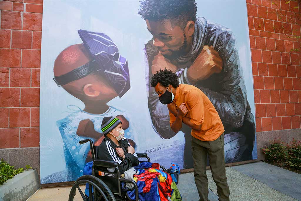 Daniel sitting in wheelchair and Nikkolas Smith in front of King Chad Mural at CHLA