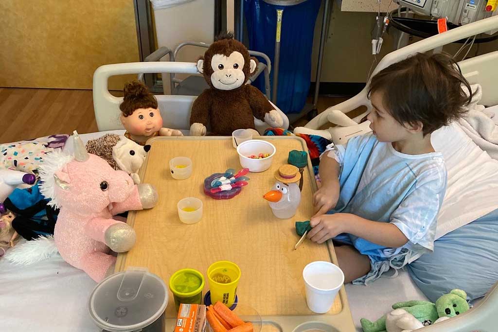 Emme sitting at hospital bed table with her stuffed animal friends